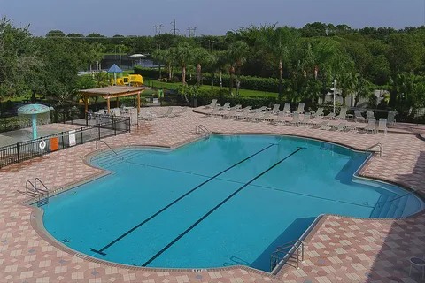 Large outdoor community swimming pool surrounded by loungers and palms