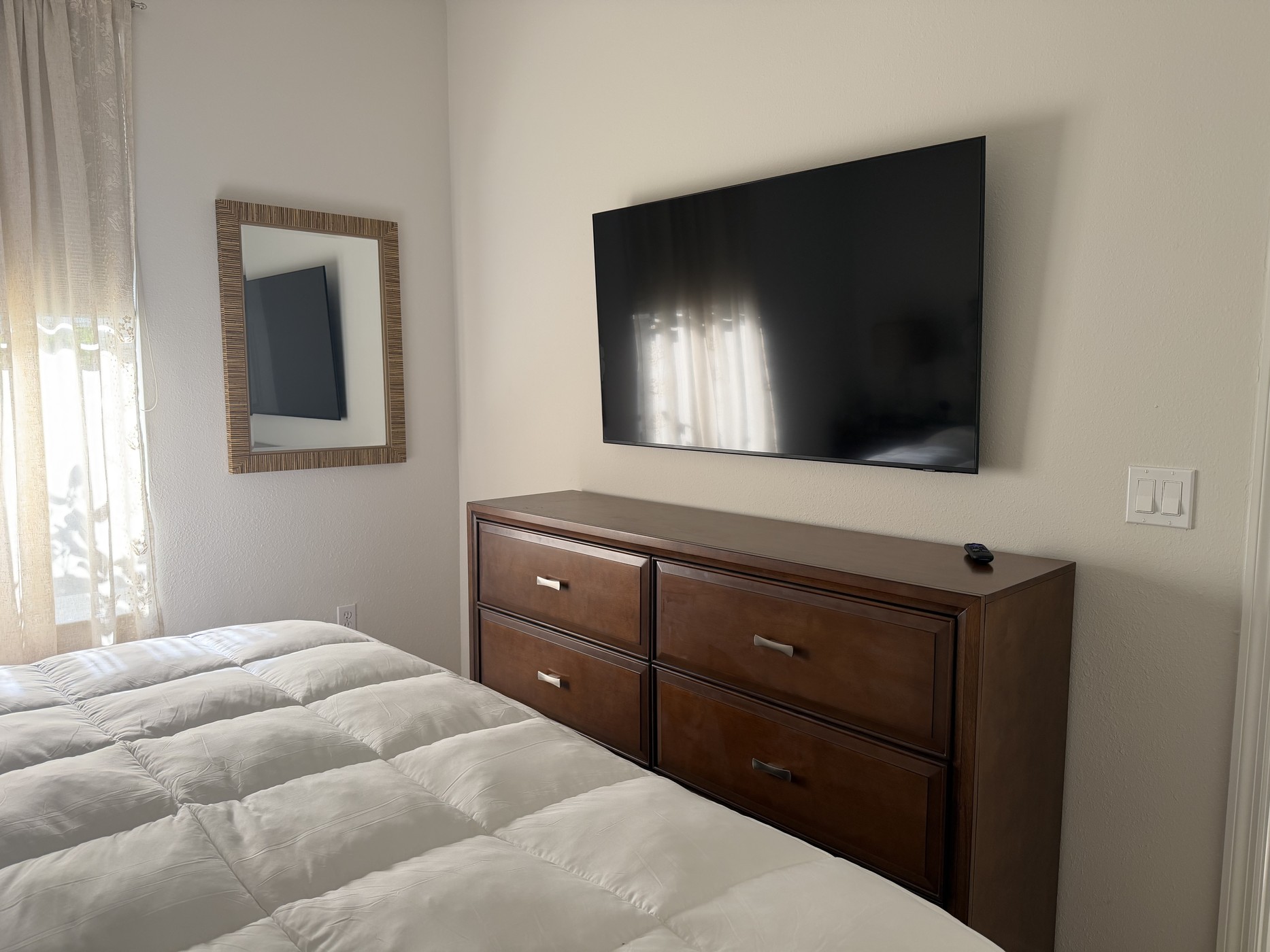 Guest bedroom with wall-mounted television, dresser, and softly filtered daylight