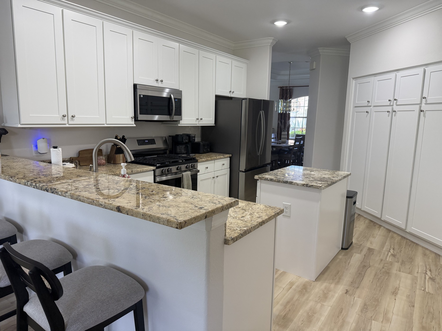 Bright white kitchen with granite counters, stainless appliances, and breakfast-bar seating