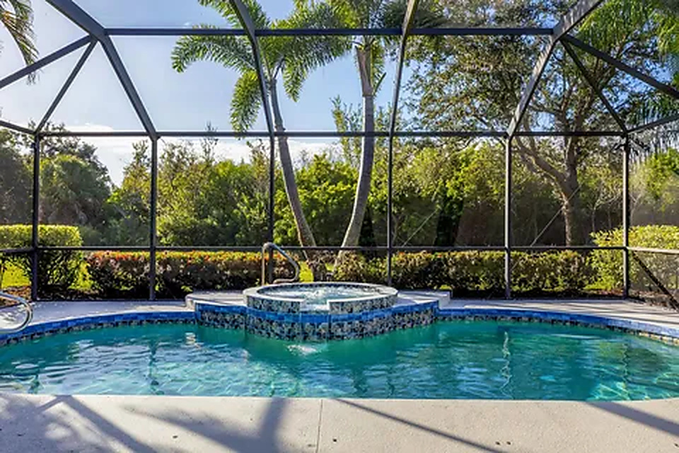 Pool and raised spa overlooking tropical greenery within the screened lanai