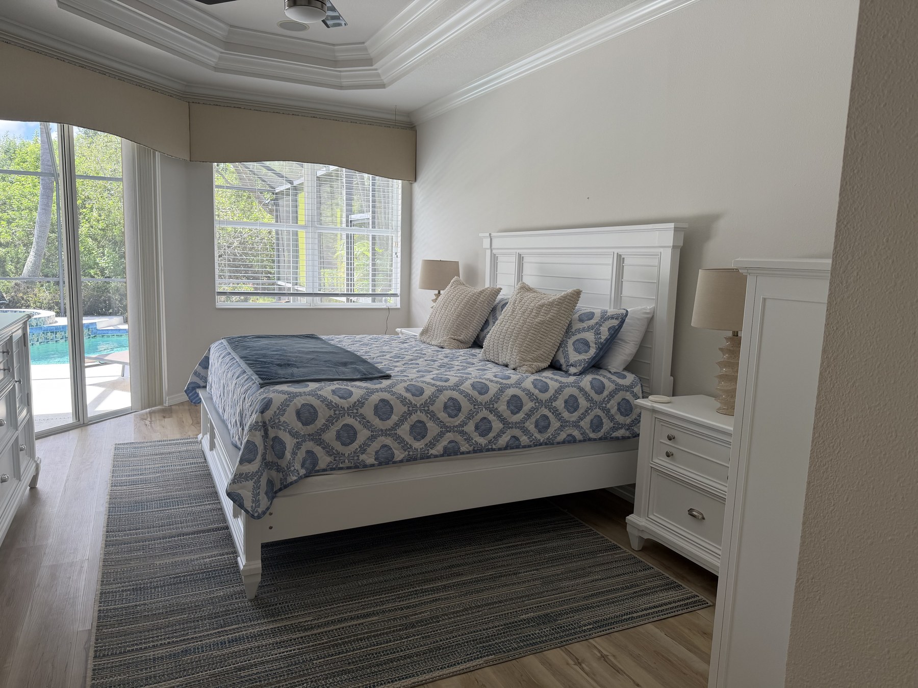 Primary suite with king bed, coastal blue linens, tray ceiling, and direct pool access